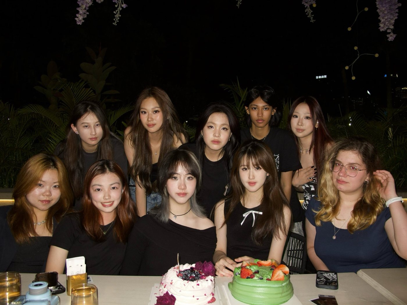 A long table of friends with two birthday cakes