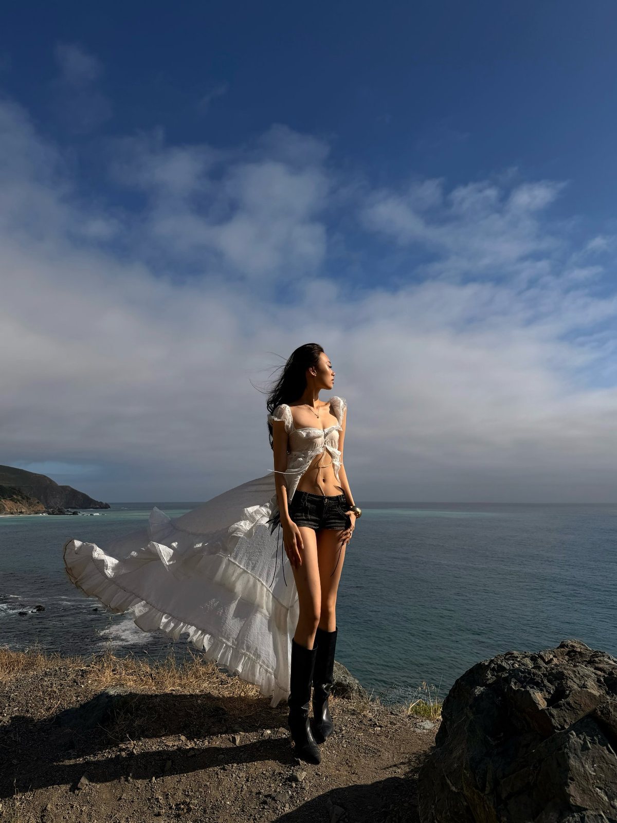 Standing on a cliff above the sea with a white dress catching the wind